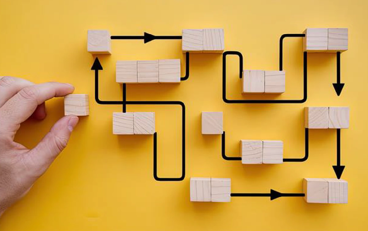 Hand holds a small wooden cube to place into a maze drawn on a yellow background.